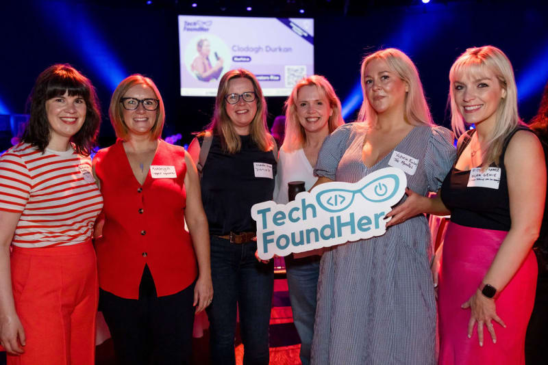 Six women pose together at the TechFoundHer Summit Dublin, one holding a large Tech FoundHer branded sign.