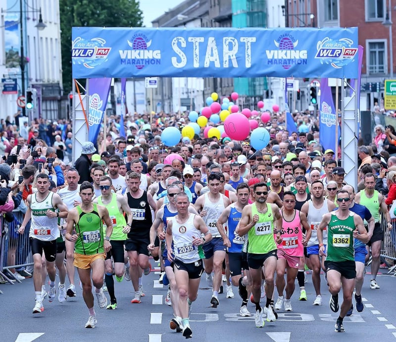 Hundreds of runners crossing the start line of the Waterford Viking Marathon beneath a blue WLR FM branded arch.