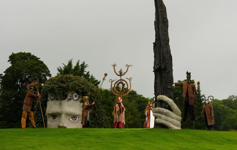 Samhain in the Heartlands costumed performers with nature masks and ceremonial props at an outdoor sculpture garden.