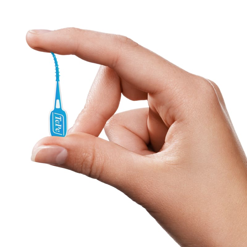 Hand holding a small blue TePe EasyPick interdental brush between thumb and index finger against white background.