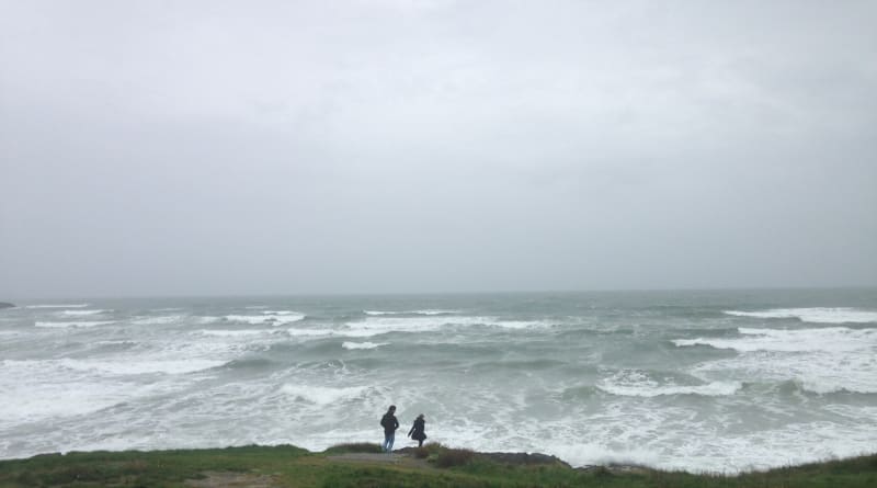 Two people stand on a cliff overlooking a stormy, wave-filled sea on an overcast winter day at Inchydoney Island.